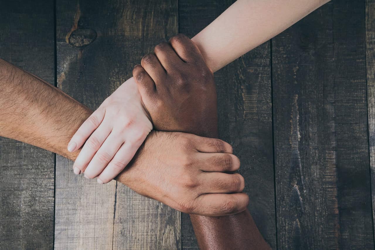 Four hands of different people clasped together in unity